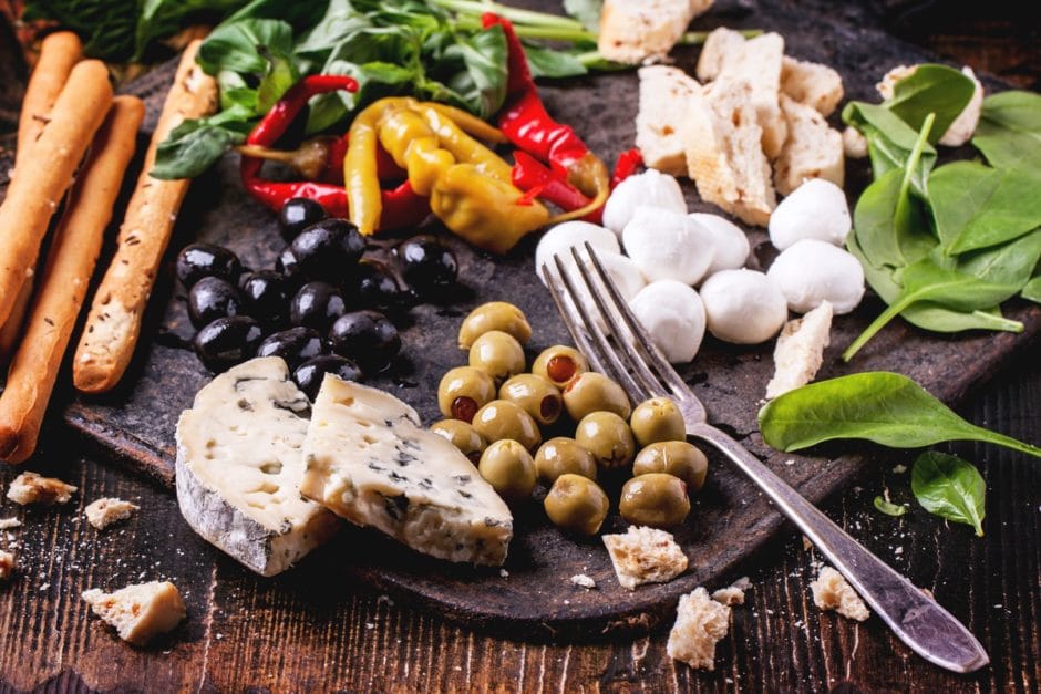 Mixed antipasti pickled blue cheese, olives and mozzarella served on cast-iron board over wooden table with vintage fork.