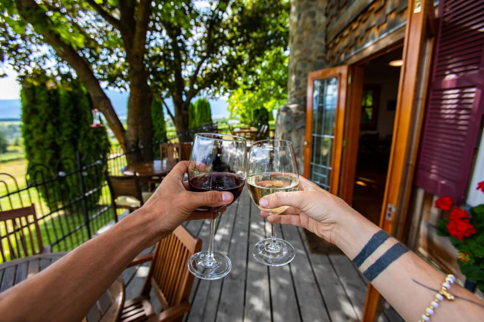 happy lovers couple hands toasting red and white wine glasses, selective focus, wine drinking, tasting in winery vineyard farmhouse terrace background.