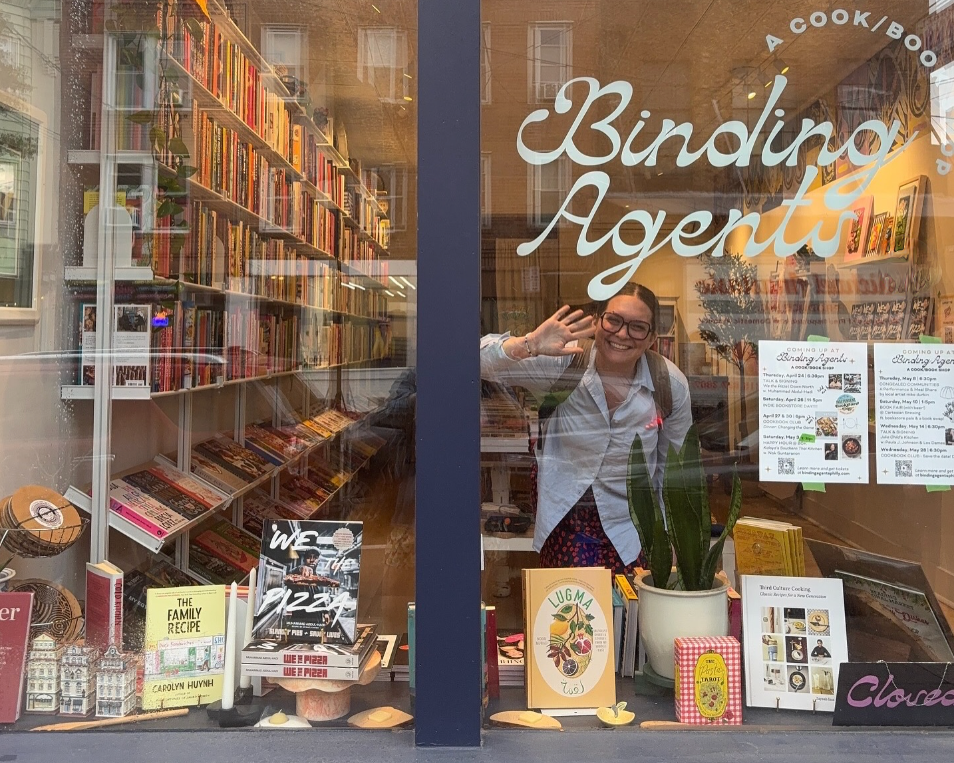 Catie Gainor waving from inside her cook/book shop, Binding Agents.