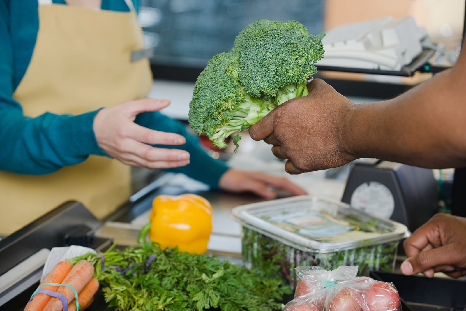 Customer handing a sales assistant broccoli.