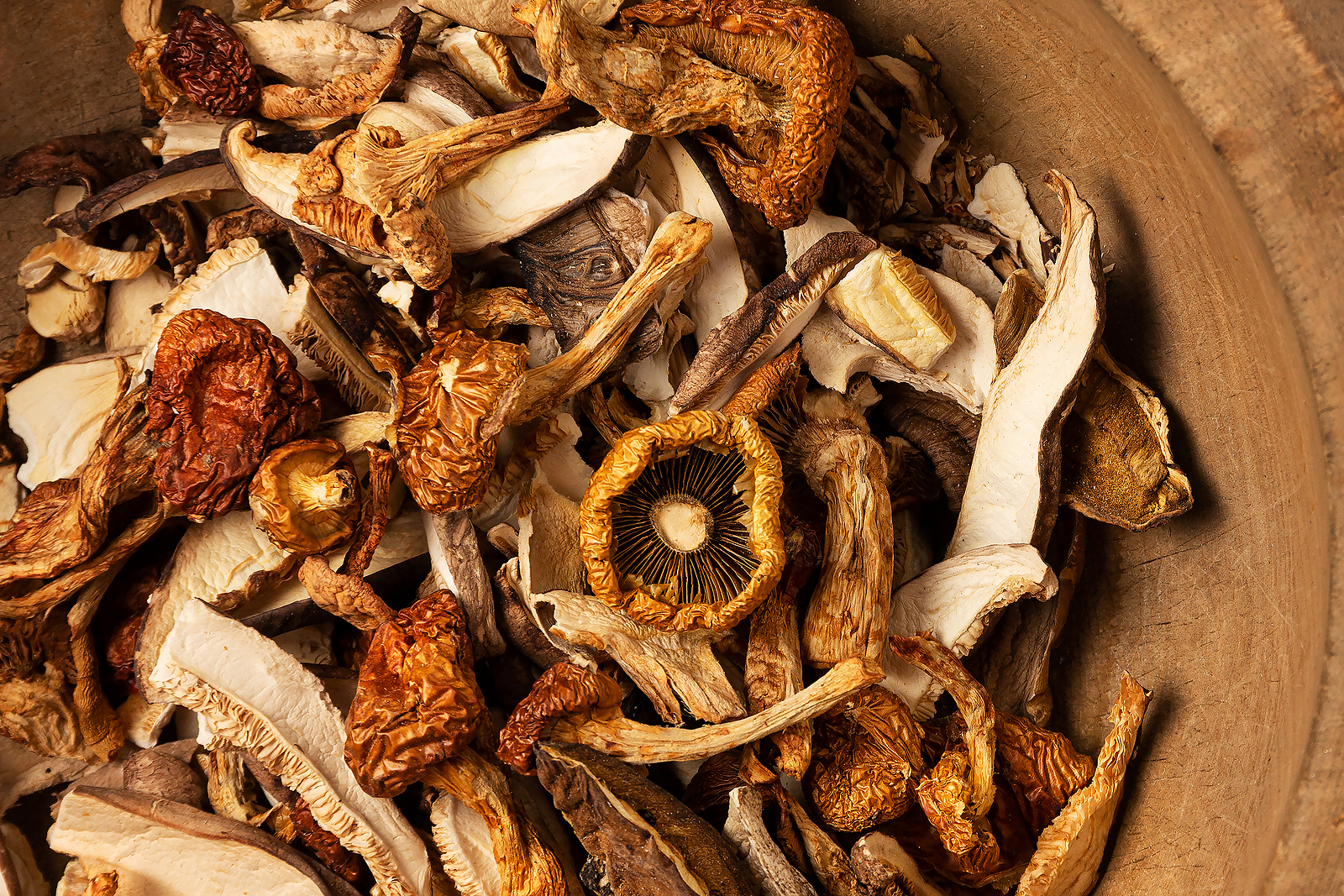 Mixture of dried chopped mushrooms in an old rustic carved wooden plate or bowl.