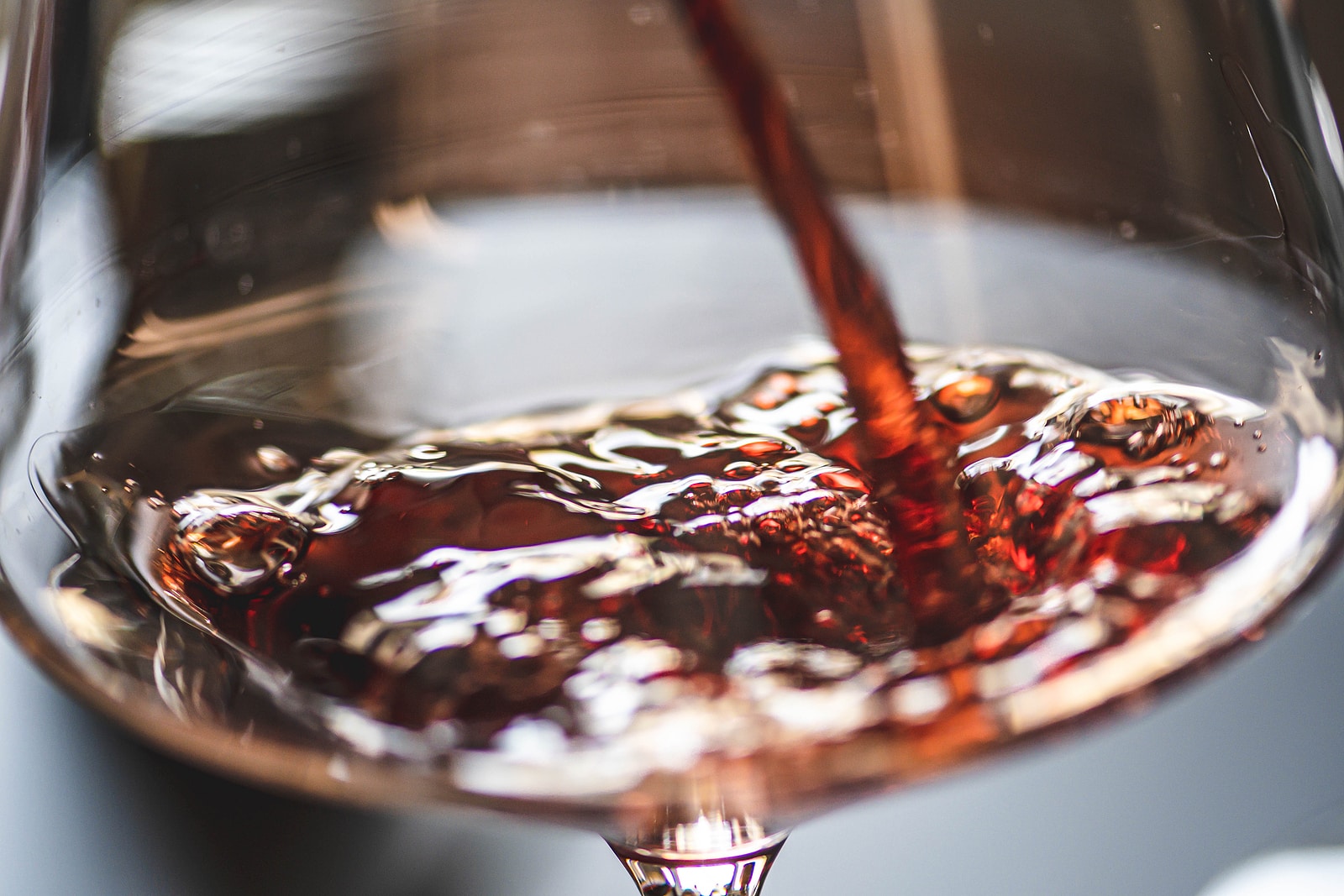 Pouring red wine into a wine glass with bubbles, close up.