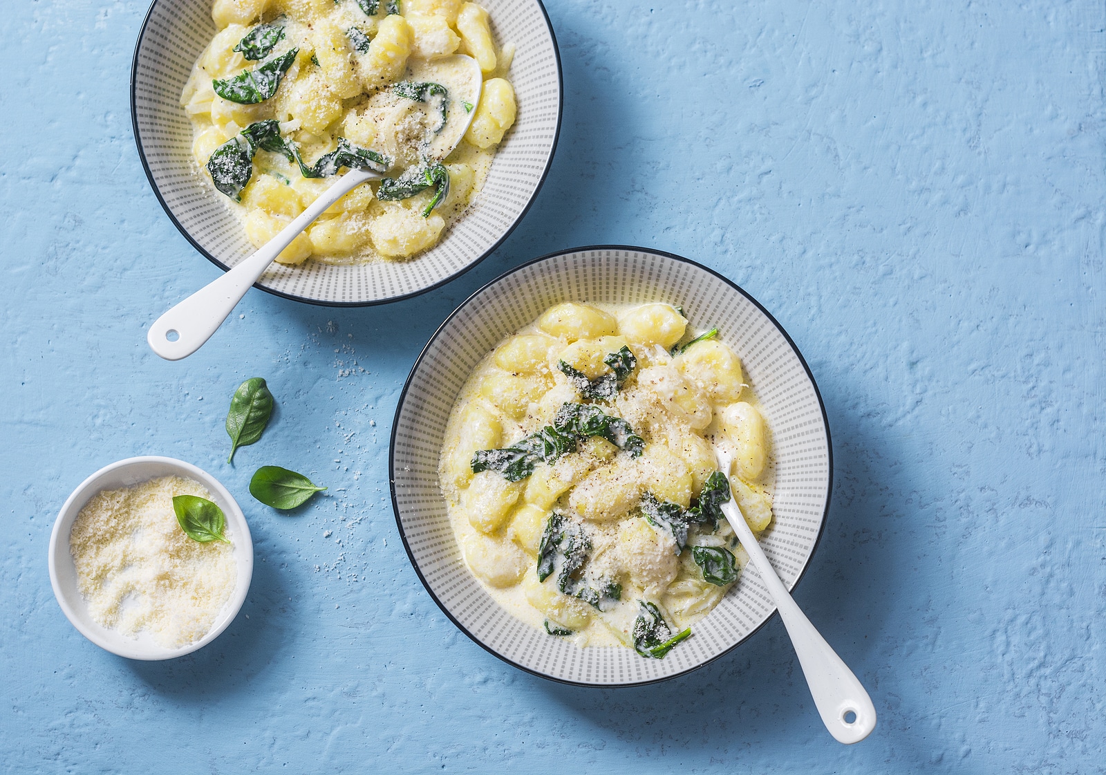 Creamy cheesy spinach potato gnocchi on a blue background top view. Mediterranean food style
