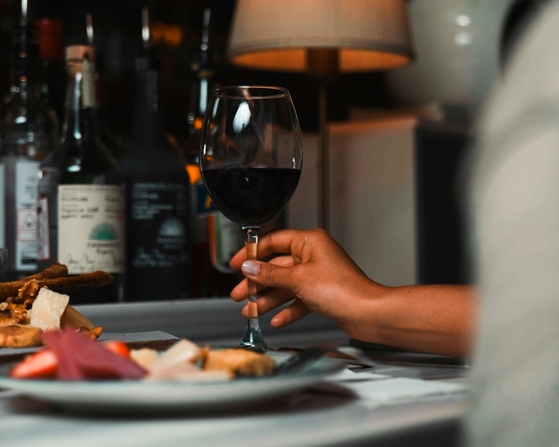 A hand holding red wine next to food.