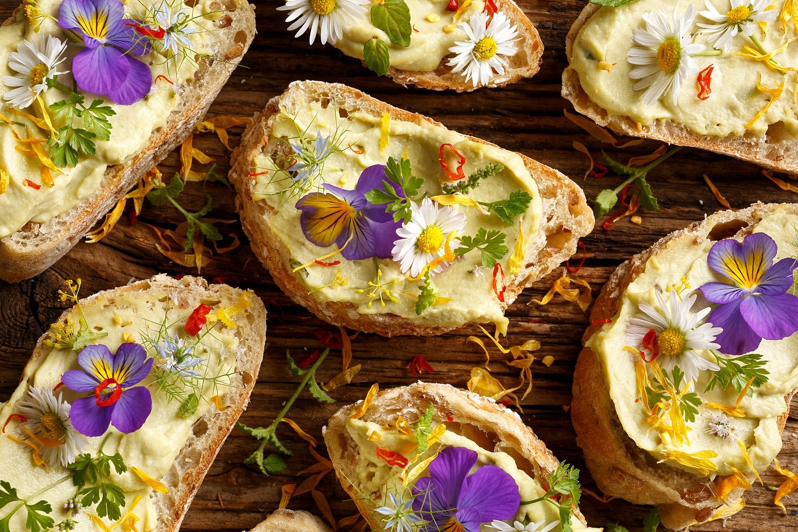 Canapes with eddible flowers and broad bean hummus on a wooden table, top view
