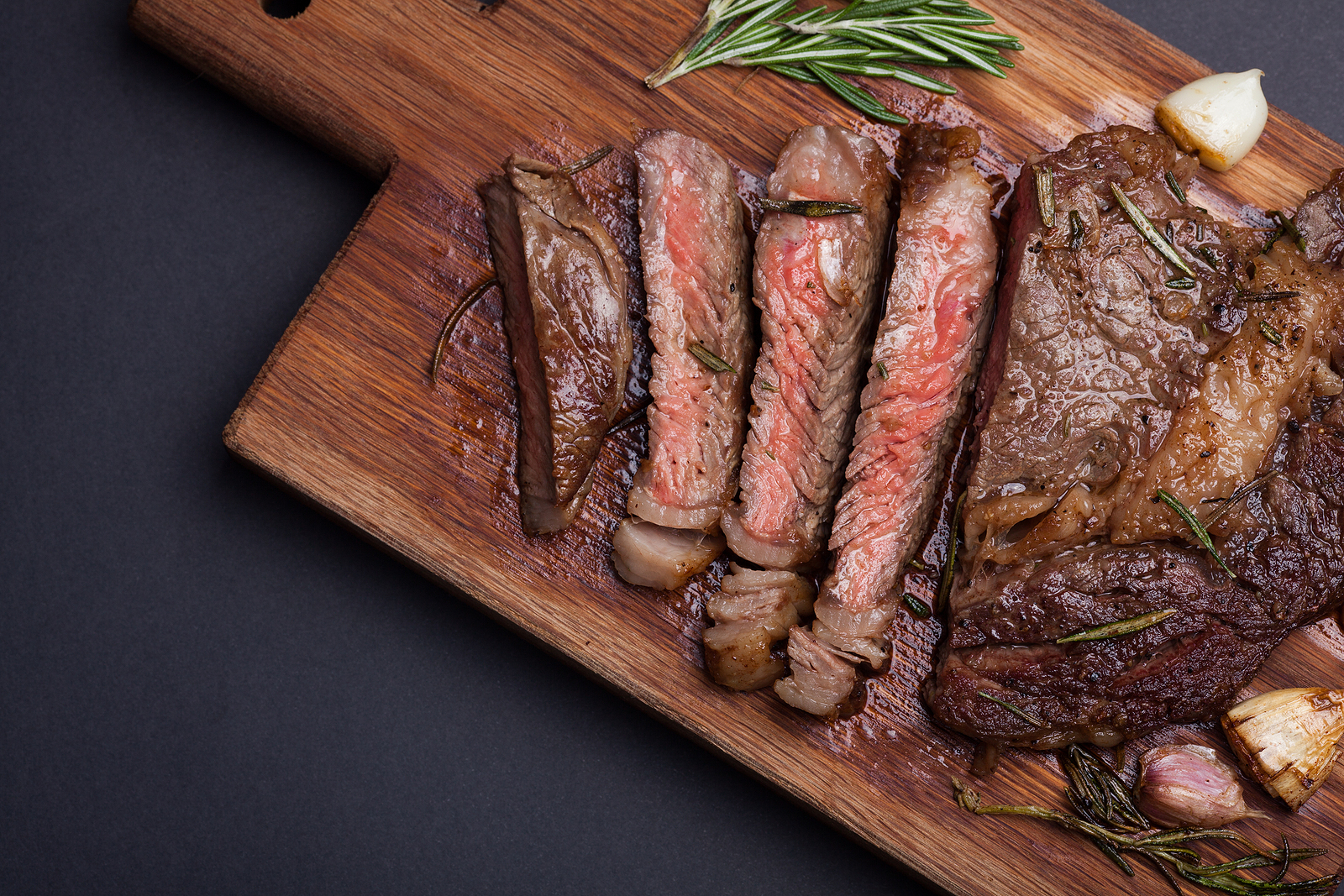 Grilled rib-eye steak of marble beef closeup with spices on a wooden Board. Juicy steak medium sliced and ready to eat. 